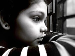 A young child looking out the window, appearing deep in thought, symbolizing childhood trauma.