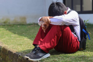 A kid sitting alone with their head down, symbolizing the emotional impact of trauma.