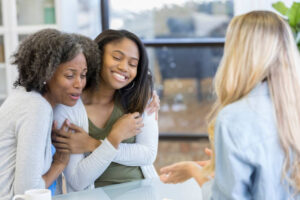 African American mom and her teenage daughter embrace after therapy session.