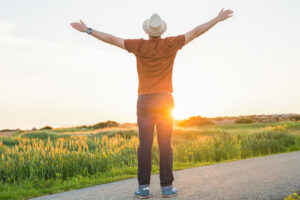 Photo of a man standing outside during the sunset with his arms stretched to the sky feeling free. Tired of trying to find time to go to therapy? With online therapy in Macon, GA you can find therapy in an easy and accessible way.