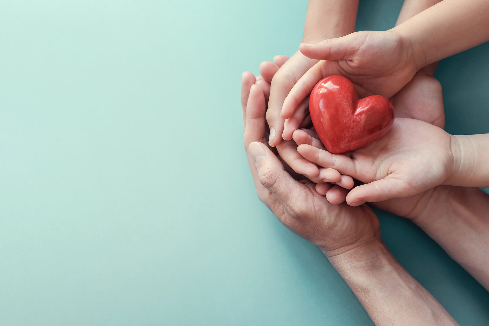 Image of a family placing their hands on top of one another and holding a red heart. Discover how PCIT therapy in Macon, GA can help you build a stronger connection with your child.