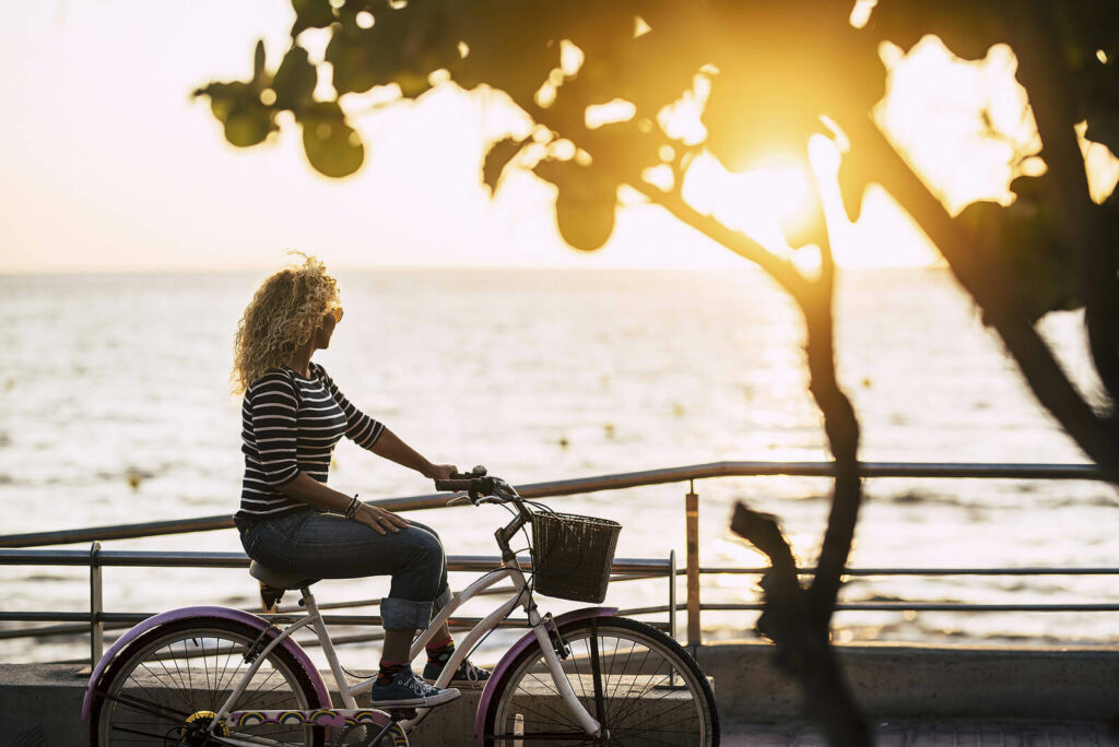 Image of a woman riding a bike near water during sunset. Discover how online therapy in Maine can help you overcome your anxiety, depression, and more!