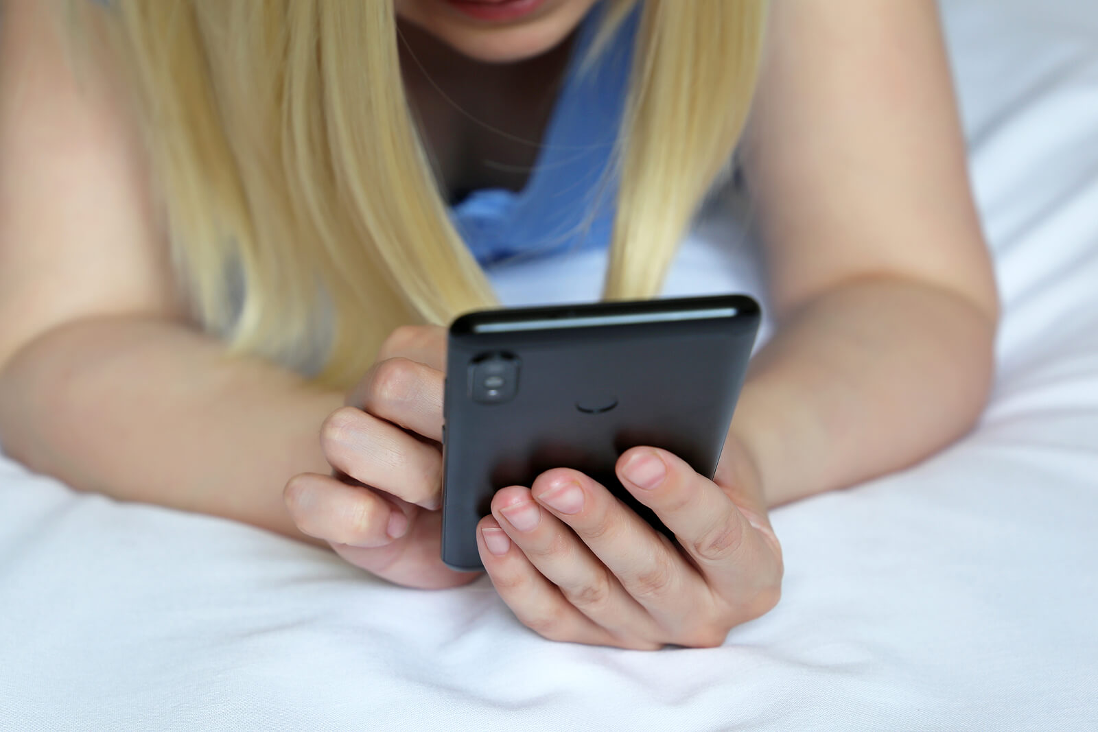 Image of a young teenage girl laying in bed holding a cell phone. Discover how social media affects your teen's mental health and how teen counseling in Macon, GA can help provide extra support!