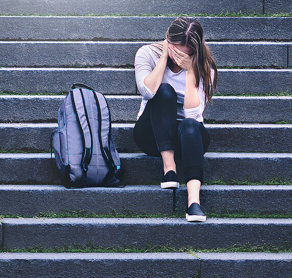 Image of a young teen girl sitting on stairs covering her face with her hand. Learn ways to help your teen manage their anxiety with the help of teen counseling in Macon, GA.