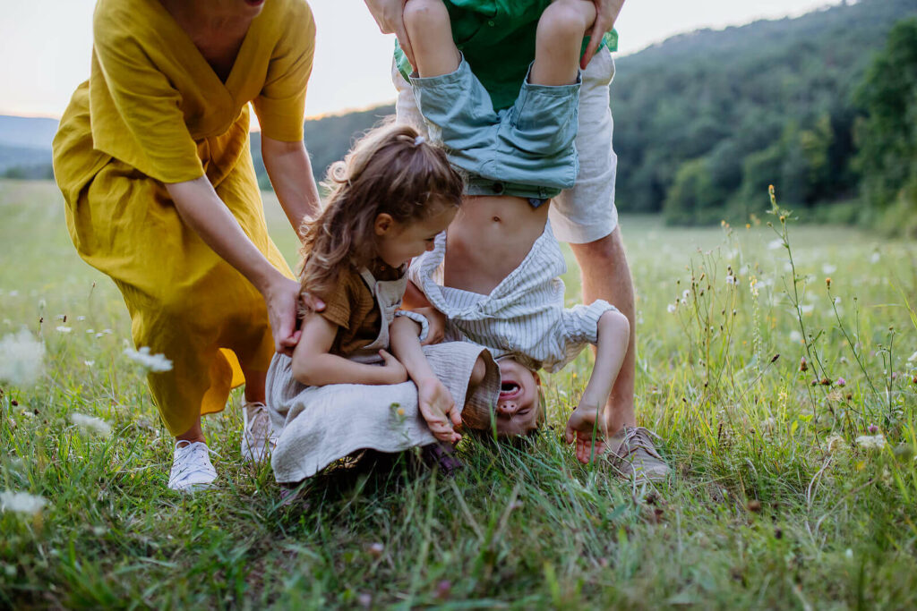 Image of two parents playing and smiling with their happy kids in a field. Find guidance when it comes to parenting and connecting with your child with the help of PCIT therapy in Macon, GA.
