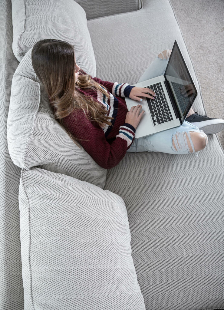Image of a young girl sitting on a couch using a laptop computer. Learn to access online therapy in Massachusetts to help overcome your trauma symptoms!