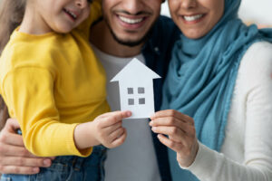 Photo of a Muslim family smiling and hugging each other while holding a paper house. Is your child struggling with their mental health? Discover how they can receive support with a skilled therapist with therapy in Hiram, GA.