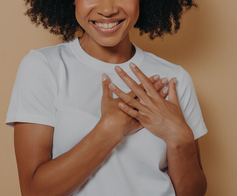 Image of a woman wearing a white tshirt and holding her hands over her heart. Learn how online therapy in Massachusetts can help you work through your anxiety, trauma, and more!