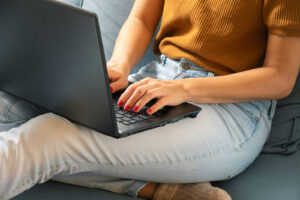 Photo of a woman sitting on a couch using a laptop to access online therapy. Learn how online therapy in Georgia can help you overcome your mental health struggles in an easy and convenient way.