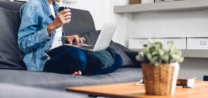 Photo of someone sitting on the couch drinking coffee and using a laptop. Are you struggling to attend therapy? Learn how online therapy in Macon, GA can help you work on your mental health in a convenient way.