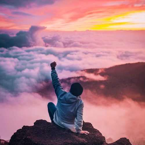 Photo of a man sitting on top of a mountain with his arm raised up in victory. Learn to work through your anger without exploding with the help of anger management counseling in Macon, GA.