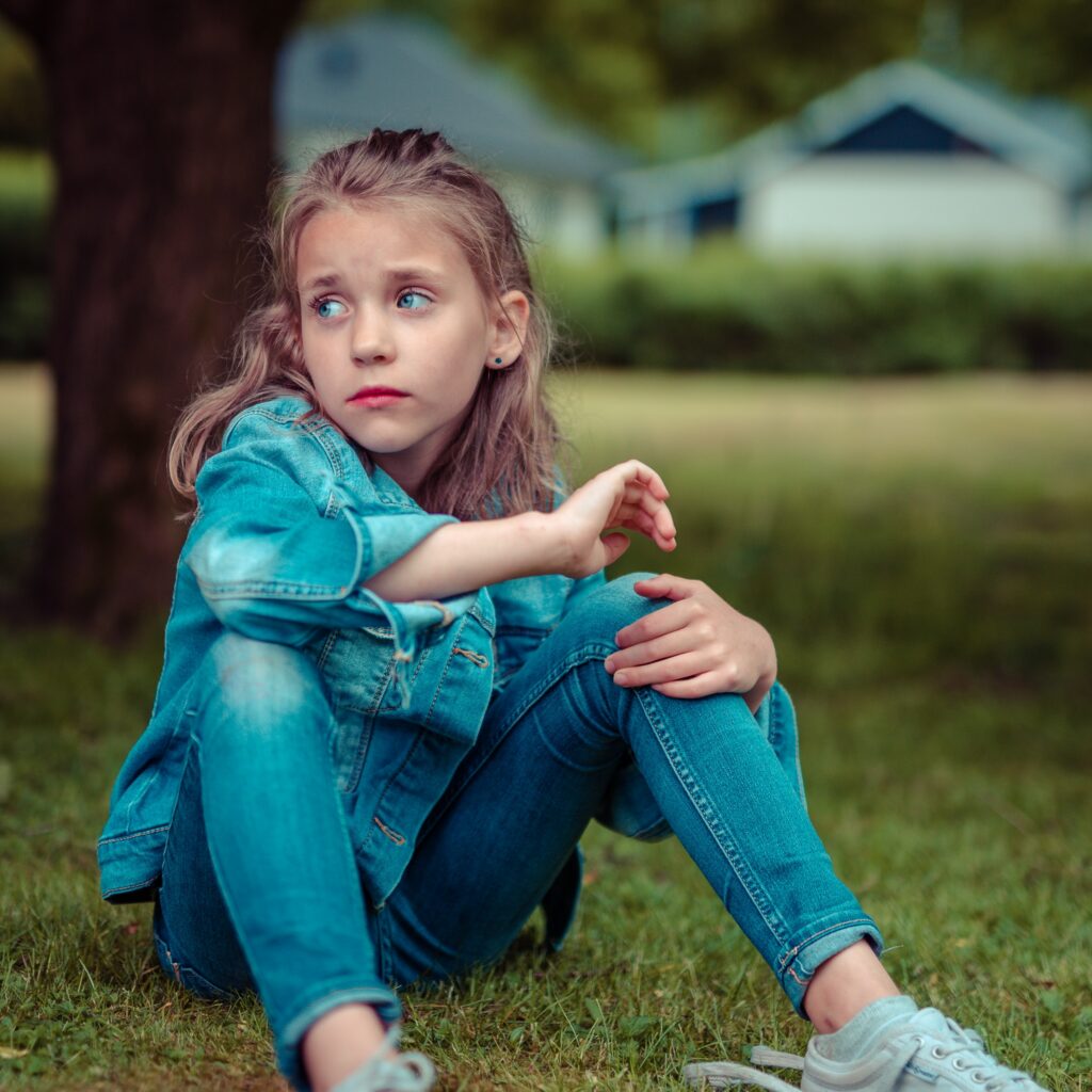 Photo of a little girl looking upset while sitting on the ground outside. Is your child struggling with anxiety, grief, or new life transitions? Discover how a trained therapist can help support your child with EMDR therapy for children in Macon, GA.