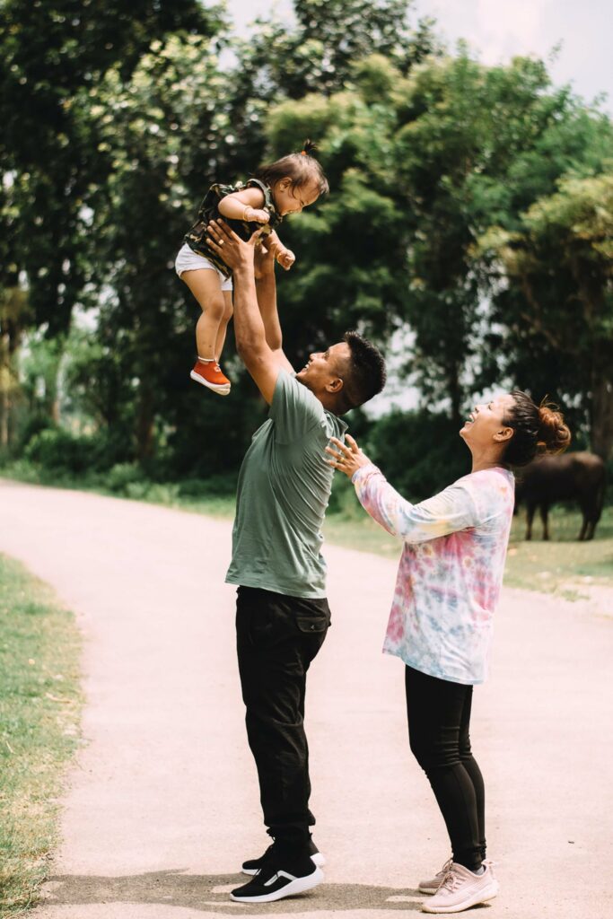 Photo of an Asian American father holding his child in the air smiling while the mother watches.