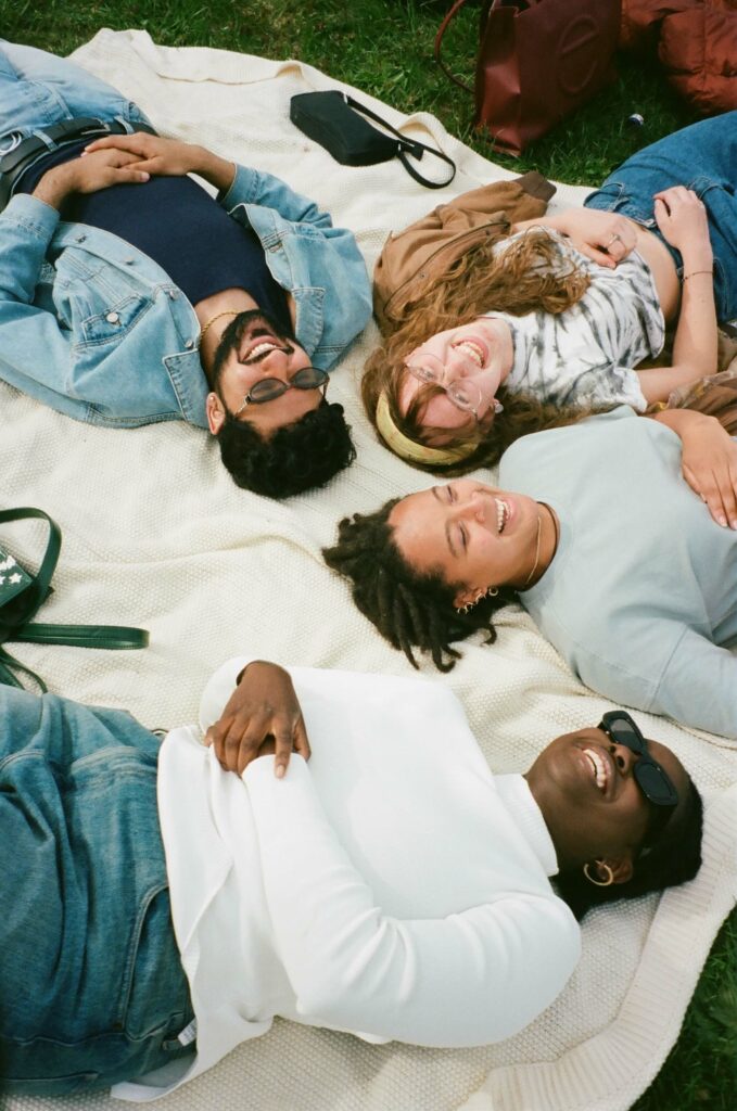 Photo of a happy group of people laying on a blanket on the ground smiling up at the sky. Find affordable mental health care with the help of The Comfy Place's sliding scale therapy in Macon, GA.