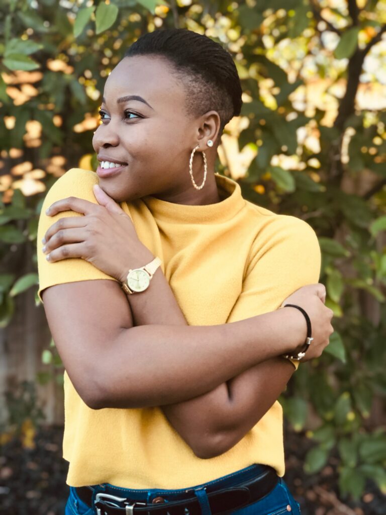 Smiling African American woman wearing a yellow shirt standing outside and hugging herself. Learn to embrace your mental health with affordable care by using sliding scale therapy in Macon, GA.
